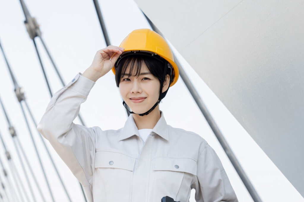 ヘルメットを被り笑顔でポーズをとる女性作業員